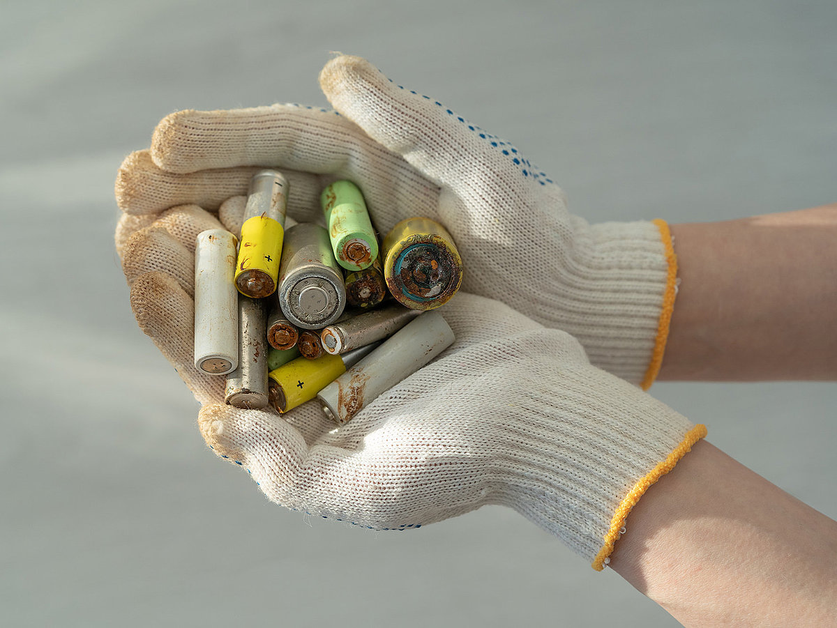 Hand mit Sicherheitshandschuh hält mehrere gebrauchte, teils beschädigte Batterien