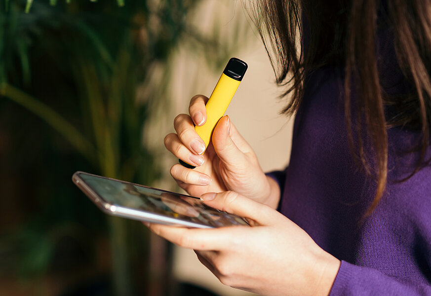 Eine Frau hält eine gelbe Vape und einen Tablet-Computer in ihren Händen.